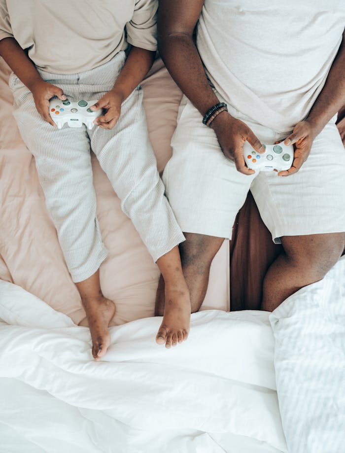 Top view of anonymous African American male and child using joysticks while playing on game console together in cozy bedroom